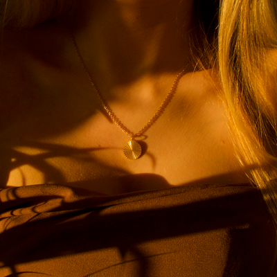Personalized round gold necklace with ribbed sunburst pattern and space for engraving of text, coordinates or handwriting on the back